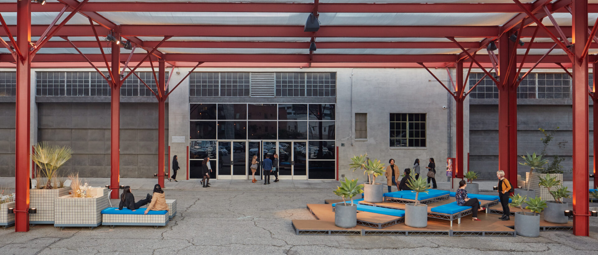 A glass-walled entrance and an open space framed by red steel beams.