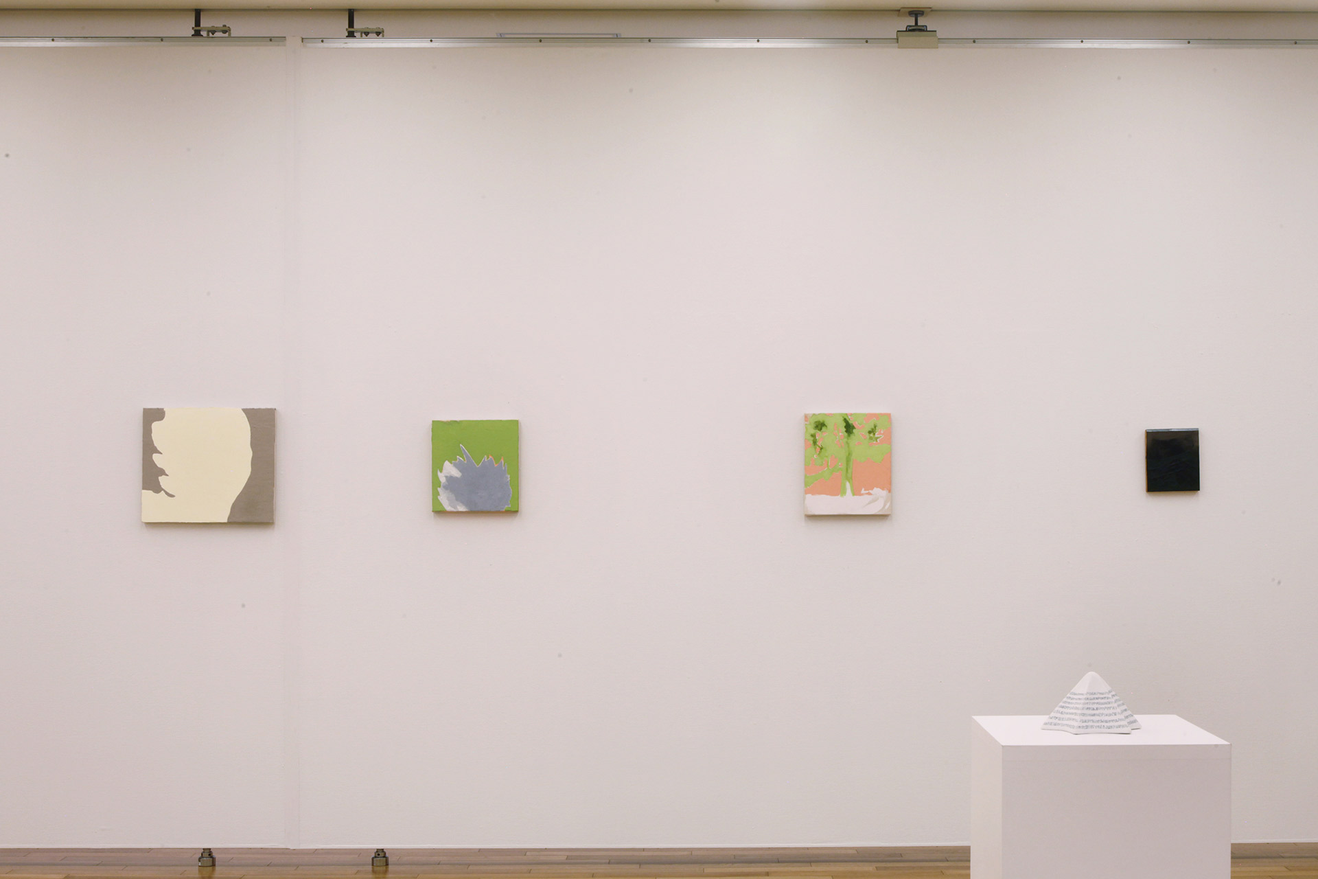 Four paintings hanging on the wall and a white three-dimensional artwork placed on a display stand.